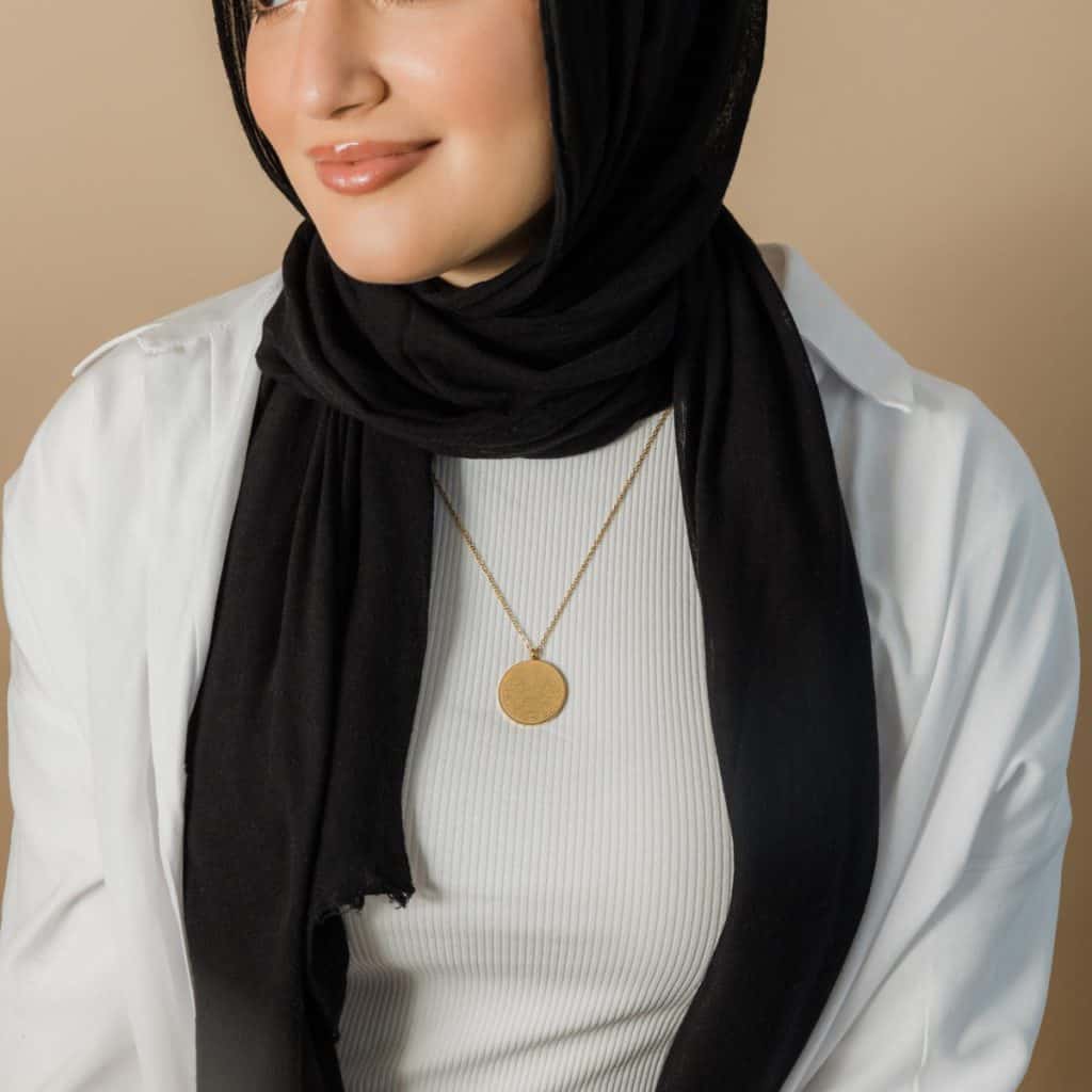Gold pendant necklace on woman wearing black hijab and white top, showcasing custom jewelry design. Perfect for elegant and personalized jewelry lovers.