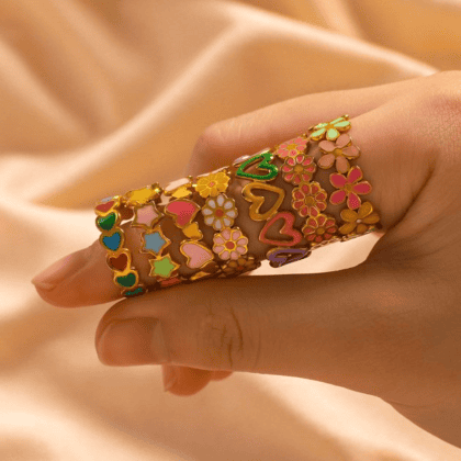 Colorful enamel floral and heart-shaped jewelry rings on a finger, showcasing custom handmade jewelry designs for women and girls, ideal for gifts and special occasions.