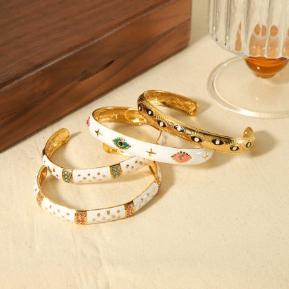 Colorful enamel and gold bangles with eye and star motifs from Nayram's custom jewelry collection displayed on a neutral surface.
