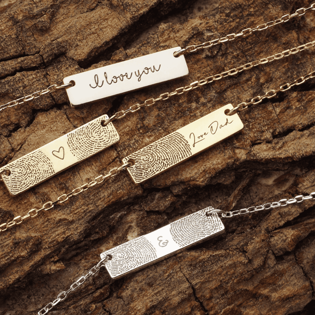 Handmade custom jewelry with engraved fingerprint designs and personalized message necklaces on rustic wood background.