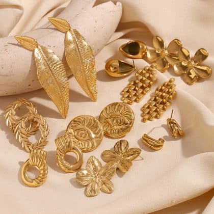 Golden leaf statement earrings, floral brooches, and chunky rings on satin fabric. Unique, handcrafted, luxury jewelry pieces emphasizing elegant design and premium materials from Nayram's custom jewelry collection.